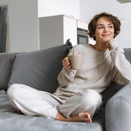 Happy young woman sitting on a couch at home, holding mug